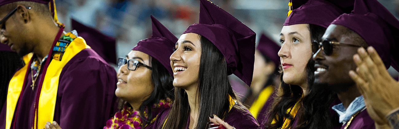Graduates in their caps and gowns smiling and clapping at commencement ceremony
