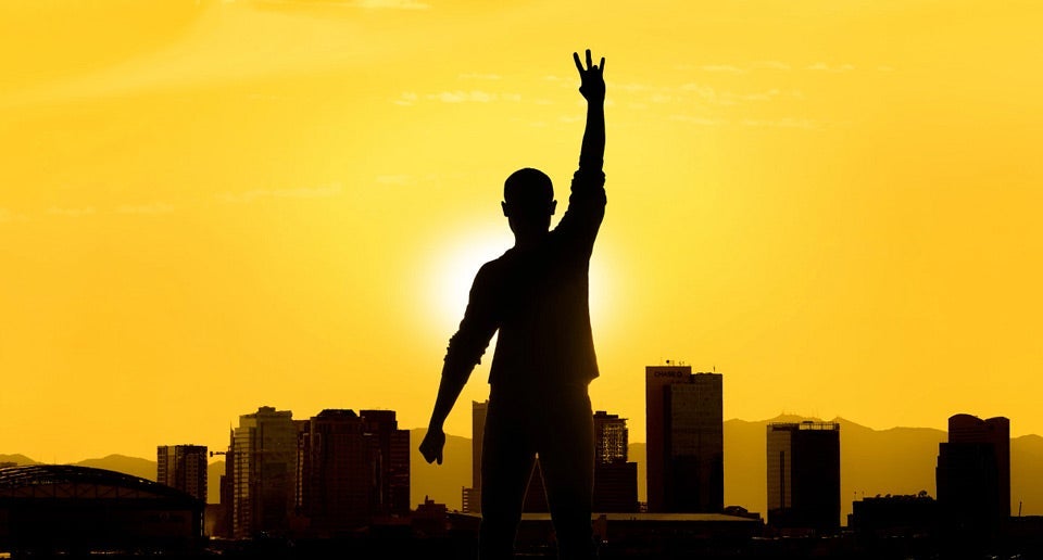 silhouette of a person doing the "Fork 'em Devils" hand sign against a golden background with ASU buildings 