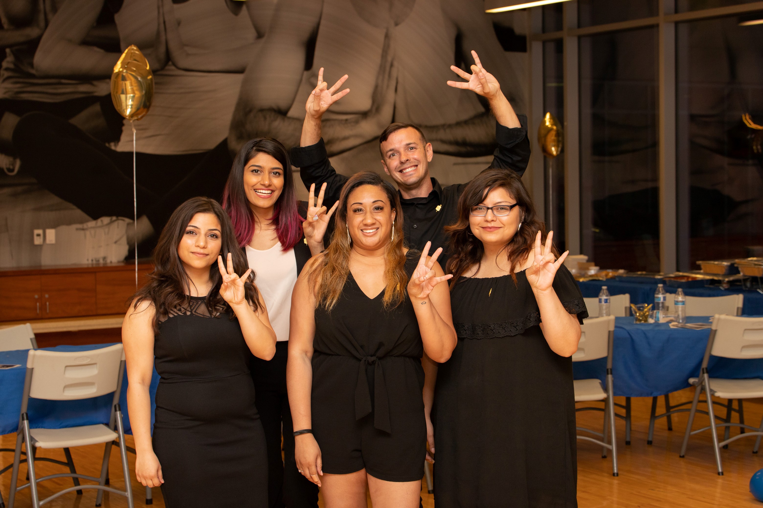five students in black formal attire posing with the "Fork 'em Devils" hand sign