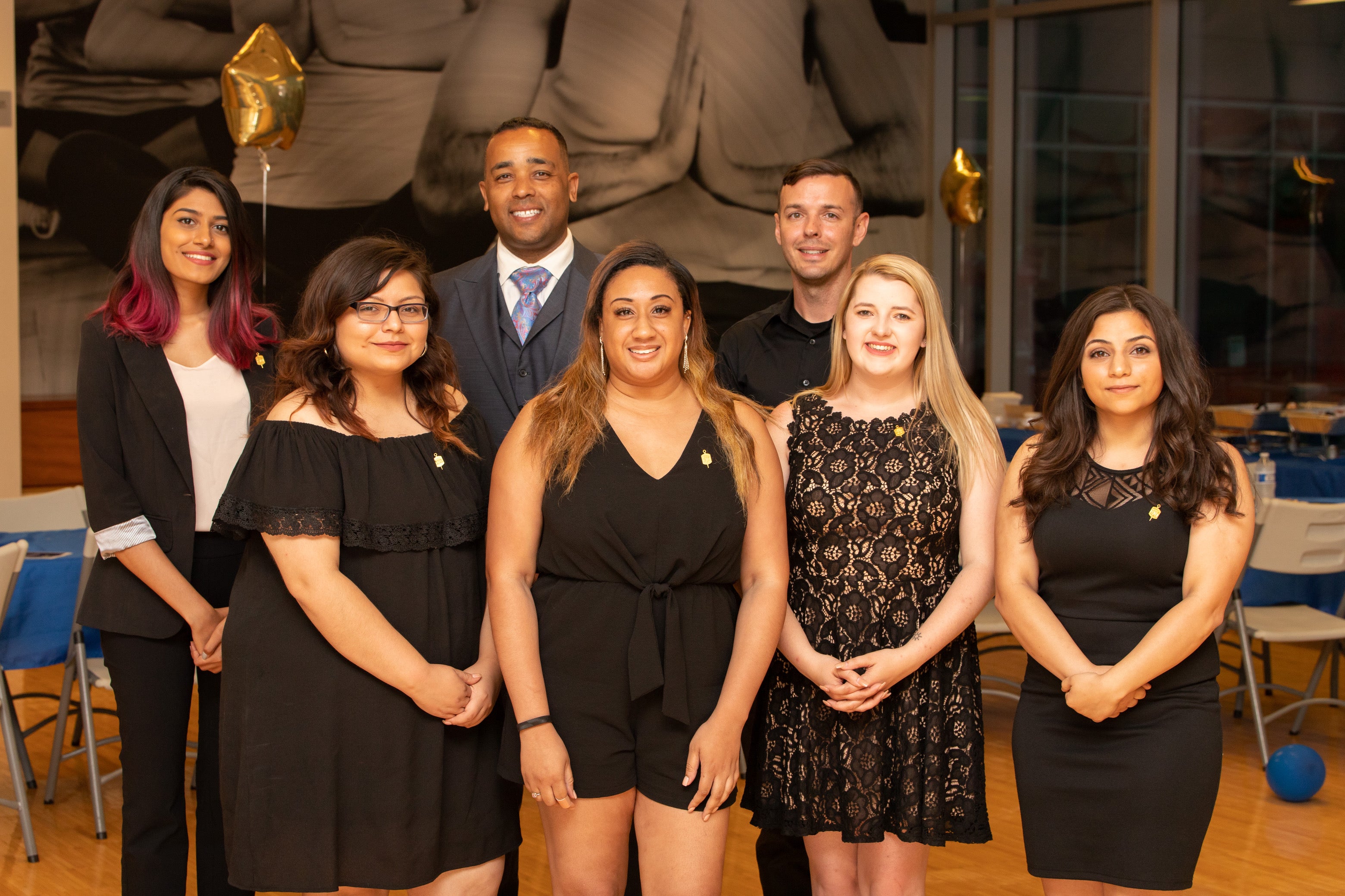 six students in black formal attire and adult male in gray suit smiling for picture